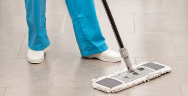 uma pessoa com calça azul limpando o pisa com um rodo