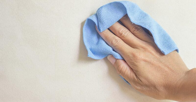 uma mão com um pequeno pano azul limpando a parede