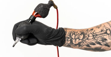 Braço tatuado com luva preta segurando máquina representando limpeza em estúdio de tatuagem.